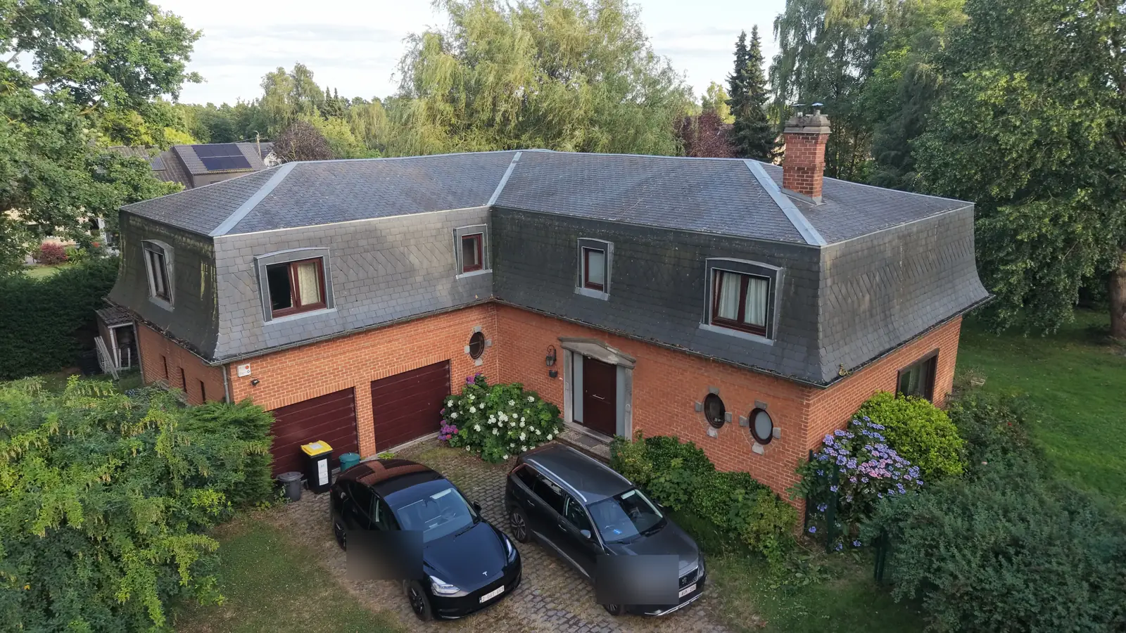 Photo aérienne par drone d'une villa quatre façades en briques et toiture d'ardoises, lumière du soir, Brabant wallon
